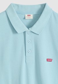 Polo Levi’s bleu clair avec trois boutons et logo Levi’s rouge sur la poitrine, taille moyenne, col ajustement standard.