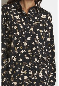 Czarna bluzka w kwiaty z guzikami, z długimi rękawami i lekko luźnym krojem. Kwiaty w stonowanych odcieniach kremowego, brązowego i zielonego.