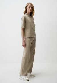 Beige ribbed knit top with short sleeves and a high neckline paired with matching wide-leg pants. White and beige sneakers complete the outfit.