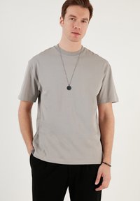 Grå kortærmet T-shirt lavet af glat stof, med en afslappet pasform, rund halsudskæring og parret med et lagdelt sølv halskæde.