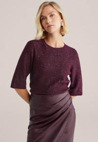 Burgundijas krāsas adīts džemperis ar īsām piedurknēm, ar teksturētu audumu un spīdīgiem akcentiem. Apvienots ar atbilstošu augsto jostas vietu ādas svārku.