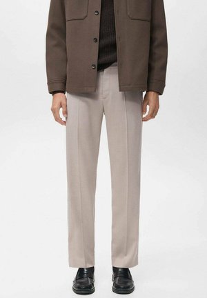 Pantalones de color beige claro con un diseño de pierna recta, pliegues en la parte delantera y una textura suave, combinados con una chaqueta marrón oscura y zapatos negros.