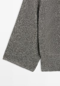 Nærbillede af ærme fra en grå strikket sweater med ribkant på en hvid baggrund.