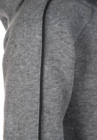 Sweatshirt gris avec un tissu texturé, doté d'un accent noir lisse le long de la couture, mettant en valeur un design et une silhouette contemporains.