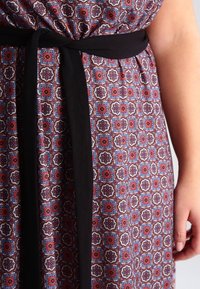 Vestido con un patrón geométrico colorido en rojo, azul y blanco, que presenta un cinturón de tela negra en la cintura y una textura suave.
