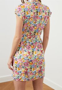 Kwiatowa sukienka z krótkimi rękawami, kołnierzykiem i dopasowaną talią. Jasne kolory obejmują różowy, żółty, niebieski i zielony. Wykonana z lekkiego materiału.