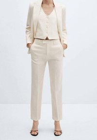 Lichtbeige linnen pak bestaande uit een getailleerde blazer, een korte tanktop met knopen en een op maat gemaakte broek. Minimalistisch ontwerp, gladde textuur.