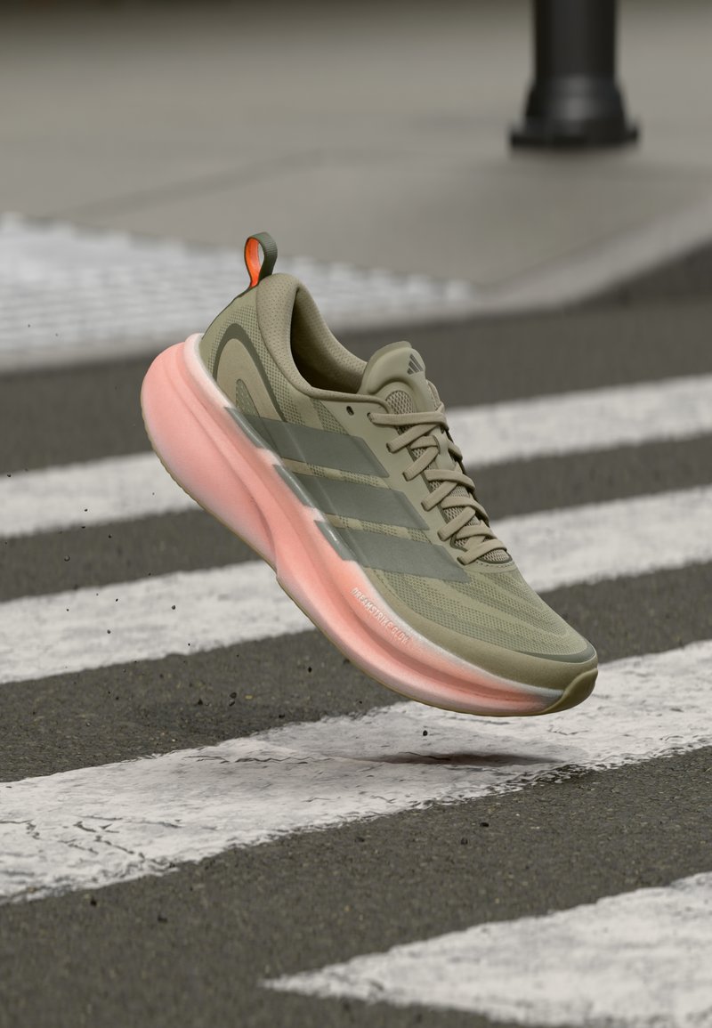 Μπεζ και ροζ αθλητικό παπούτσι Adidas να αιωρείται πάνω από μια υγρή διάβαση πεζών με μικρές σταγόνες νερού από κάτω.