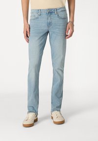 Light blue denim jeans with a straight cut, five-pocket design, and subtle fading. Worn with cream shoes featuring brown soles.