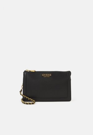 Pochette Guess noire pour poignet avec fermeture éclair dorée et sangle chaîne, avec le nom de la marque et "EST 1981" en lettres dorées à l'avant.