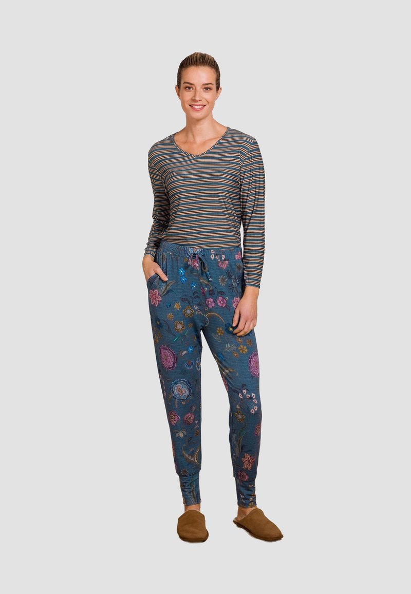 Langsleeve gestreepte top in blauw, gecombineerd met blauwe bloemen joggerbroeken met zakken en een elastische tailleband. Bruine instap schoenen.