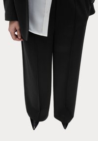 Schwarze maßgeschneiderte Hose mit geradem Beinschnitt und Bügelfalte, kombiniert mit einem weißen Hemd und spitzen schwarzen Stilettos.