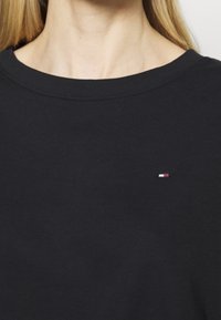 Suéter negro de algodón de cuello redondo con un pequeño logo blanco, rojo y azul en el pecho. Textura suave y ajuste estándar.