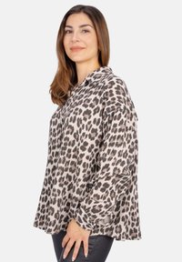 Bluse mit Leopardenmuster, Kragen und lockerer Passform. Weicher Stoff mit schwarzen und braunen Flecken auf einem hellbeigen Hintergrund.
