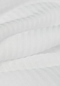 Tissu blanc côtelé avec une texture douce, présentant des rayures alternant entre en relief et plates. Le matériau semble léger et respirant.