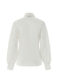 Blusa bianca con colletto classico, dotata di maniche a palloncino ricamate e trasparenti. Tessuto liscio con delicati motivi floreali sulle maniche.