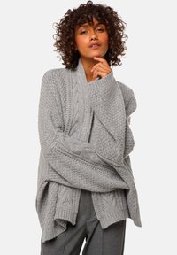 Pull en maille gris avec une texture épaisse, présentant des motifs en torsades et côtes, au design surdimensionné et aux manches larges.