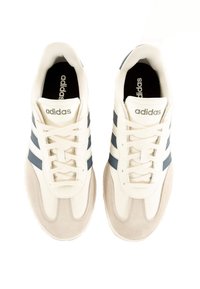 White athletic sneakers with navy blue stripes, suede accents, and a textured rubber sole. Features laces and an Adidas logo on the tongue.