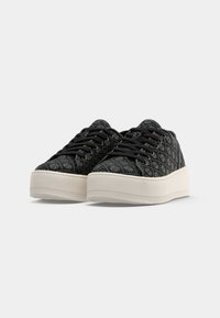 Sneaker nere con motivo a stampa e design testurizzato, dotate di suola piatta bianca e lacci neri. Gli accenti includono un motivo logo ripetuto sulla tomaia.