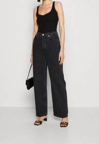 Černý žebrovaný top bez rukávů, černé džíny s vysokým pasem a širokými nohavicemi, černé sandály na klínku se zlatými detaily a malá černá kabelka.