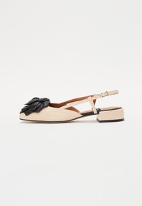 Beige slingback shoe with a black leather flower embellishment, triangular toe shape, low block heel, and adjustable ankle strap.