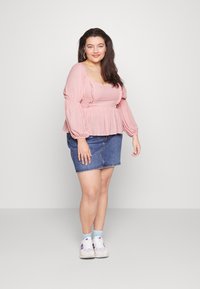 Blusa rosa de mangas longas com detalhes em babados, combinada com uma saia de ganga. O conjunto é complementado por ténis brancos e meias azul clarinho.