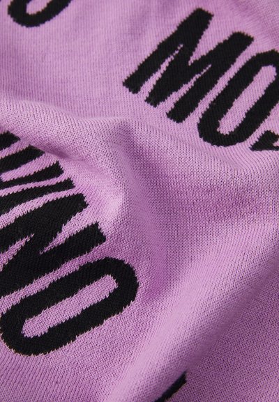 Lila kötött anyag, látványos fekete szöveggel. Simag textúra, a kiemelkedő feliratok kontrasztot képeznek a háttérrel.