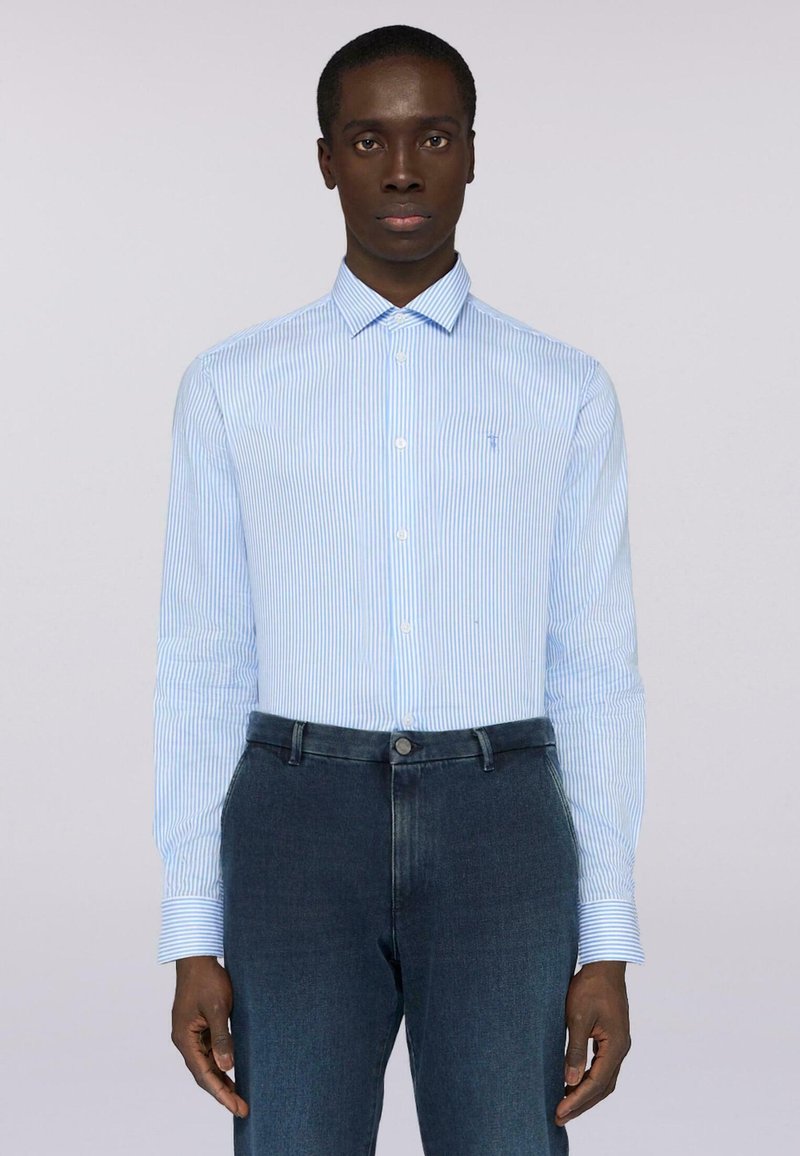 Modrá pruhovaná košile s dlouhým rukávem vyrobená z bavlny, s límcem na knoflíky a malým logem na hrudi, kombinovaná s tmavými džínovými kalhotami.