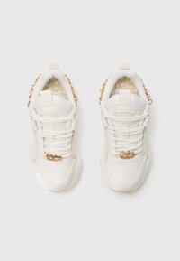 Hvide sneakers med et klodset design, der har en tekstureret overflade, gyldne metaldele og en dekorativ kædediend på hælen.