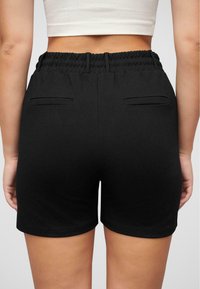 Sorte shorts med elastisk linning, to baklommer og en glatt tekstur. Kanten er avrundet uten ekstra dekor.