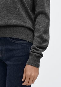 Dunkelgrauer Strickpullover mit geripptem Saum und Bündchen, kombiniert mit dunkelblauen Jeans, zeigt eine glatte Textur und eine enganliegende Passform.