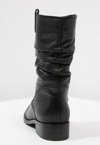 Czarne skórzane botki za kostkę o opadającym kroju, zaokrąglony czubek, niski obcas i widoczne detale przeszycia. Prostokątny uchwyt na górze.