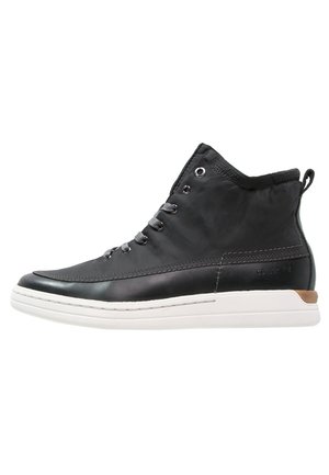 Baskets montantes noires avec lacets gris, semelle blanche et accent marron au talon, présentées de profil sur fond blanc.