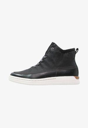 Baskets montantes noires avec lacets gris, semelle blanche et accent marron au talon, présentées de profil sur fond blanc.