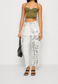 Olivgrön kort topp med spetsdetaljer, kombinerad med högmidjade vita jeans med svarta stänk och svarta snörsandaler.