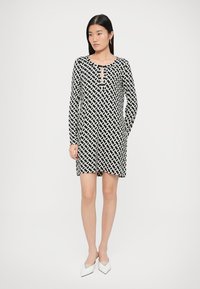 Juoda ir balta raštuota suknelė su ilgomis rankovėmis, kelio ilgio, su iškirpte prie kaklo ir šoninėmis kišenėmis. Medžiaga lygi ir turi minkštą tekstūrą.