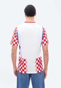 Mies, jolla on valkoinen paita, jossa on punaruudulliset hihat ja alaosa, seisoo selin, yhdistettynä sinisiin farkkuihin.