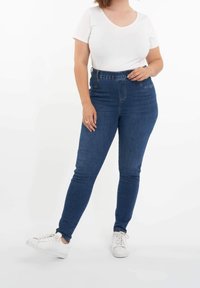 Korkeavyötäröiset, tummansiniset denim-farkut, joissa on slim fit -leikkaus, etutaskut ja joustava vyötärönauha, yhdistettynä lyhythihaiseen valkoiseen puseroon.