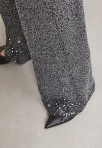Grijze wijde broek van gebreid materiaal met textuur, voorzien van een zoom met pailletten en puntige zwarte schoenen.