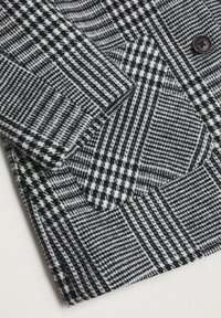 Černobílá látka s vzorem houndstooth, texturovanými designy v zigzagu a kostkovém vzoru, s jedním detailem černého knoflíku.