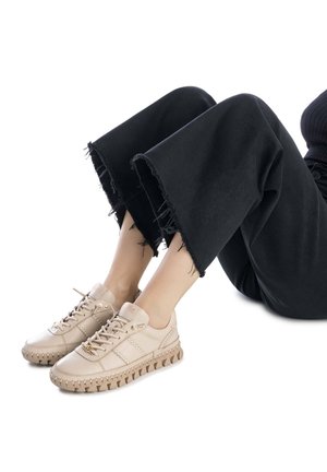 Zapatillas de cuero beige con suela texturizada, con detalles de costura y cordones, combinadas con pantalones negros de dobladillo deshilachado.