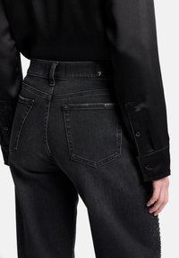 Czarne dżinsy z wysokim stanem, z klasycznym pięciokieszeniowym krojem, subtelnym przeszyciem i teksturowaną ozdobą wzdłuż boku.