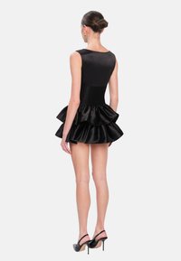 Vestido de satén negro con un corsé ajustado y una falda acampanada de volantes en capas. Diseño sin mangas, textura suave y silueta audaz.