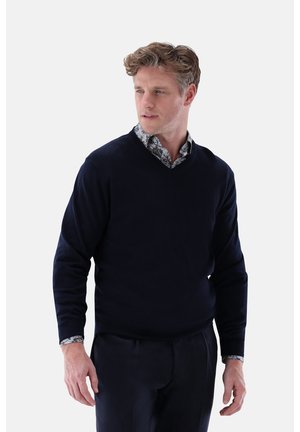 Marineblauer V-Ausschnitt-Pullover aus weichem Material mit langen Ärmeln. Darunter ist ein blumenmusterhemd am Kragen sichtbar.