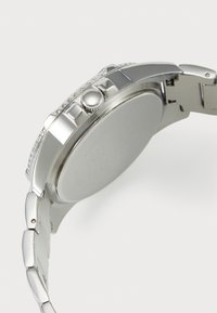 Montre en acier inoxydable argenté avec une finition polie, une lunette striée et un boîtier rond. Comprend une couronne et des maillons dans le bracelet.