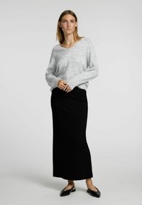 Lys grå strikket sweater med v-udskæring og lange ærmer, parret med en sort, tætsiddende, ankel-lang nederdel. Sorte flade sko fuldender outfittet.