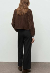 Chaqueta corta de ante marrón con mangas largas, combinada con pantalones negros de cintura alta. Textura suave y diseño minimalista.