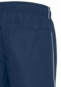 Shorts sportivi blu navy con vita elastica, strisce laterali bianche e una tasca posteriore con pattina quadrata. Tessuto dalla texture liscia.