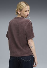 Brun ribbet corduroy t-shirt med korte ærmer og en afslappet pasform, parret med mørke denim jeans. Teksturen er fremtrædende; synlige syninger detaljer.