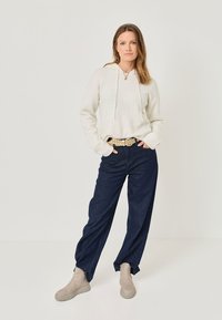 Light beige hoodie with drawstrings, paired with dark denim wide-leg pants. Soft texture, neutral tones, and a beige chunky boot with a ridged sole.